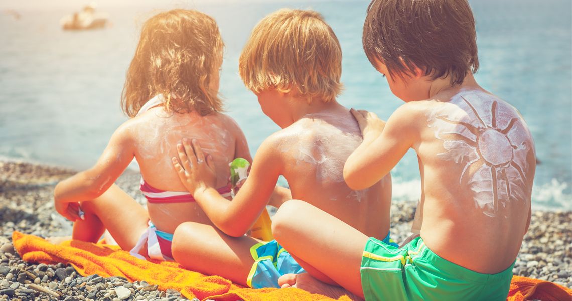 three young kids applying sunscreen to each others' backs while drawing shapes in the sunscreen