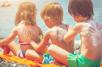three young kids applying sunscreen to each others' backs while drawing shapes in the sunscreen